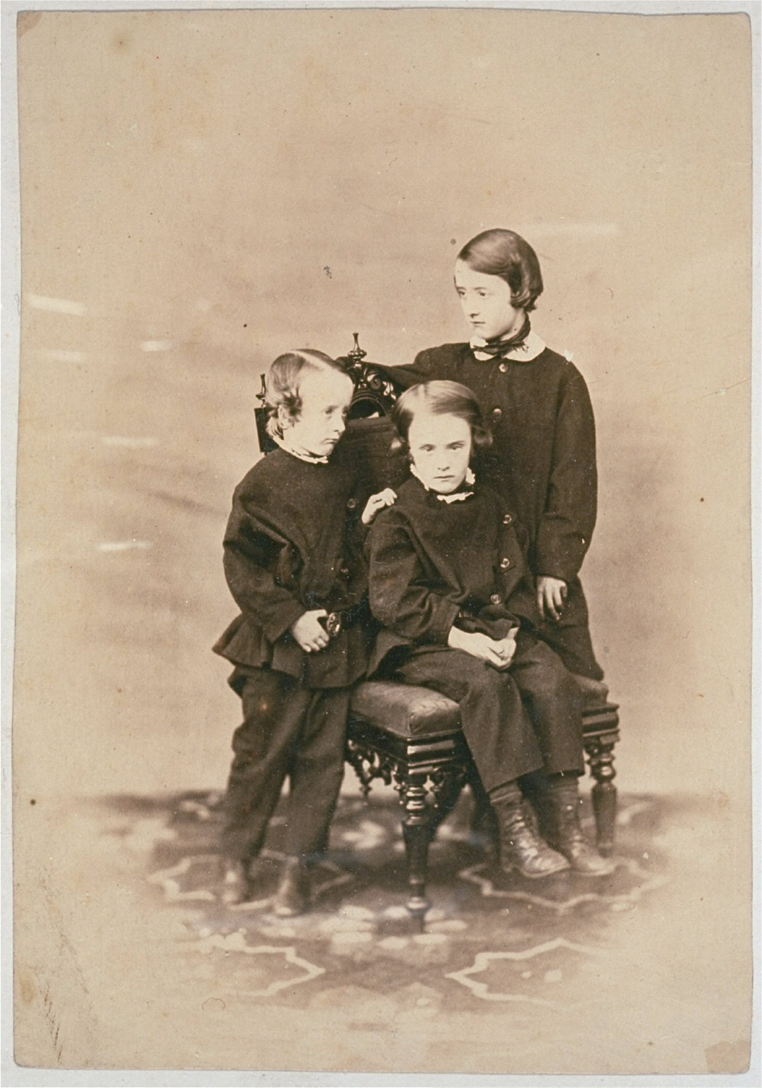 Two boys and a young girl by a carved chair